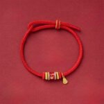 Om Mani Padme Hum copper red string bracelet with mantra beads flat lay on dark red background