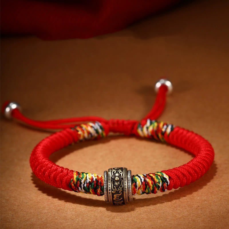 Red string Buddhist bracelet with silver rotating charm bead and colorful woven accents on brown background