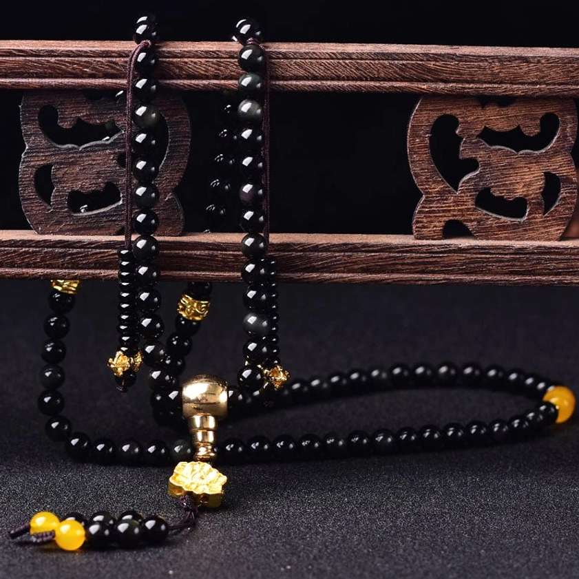 Loose 108-bead black obsidian Buddhist mala necklace with gold-tone hardware and amber beads displayed on carved wooden shelf
