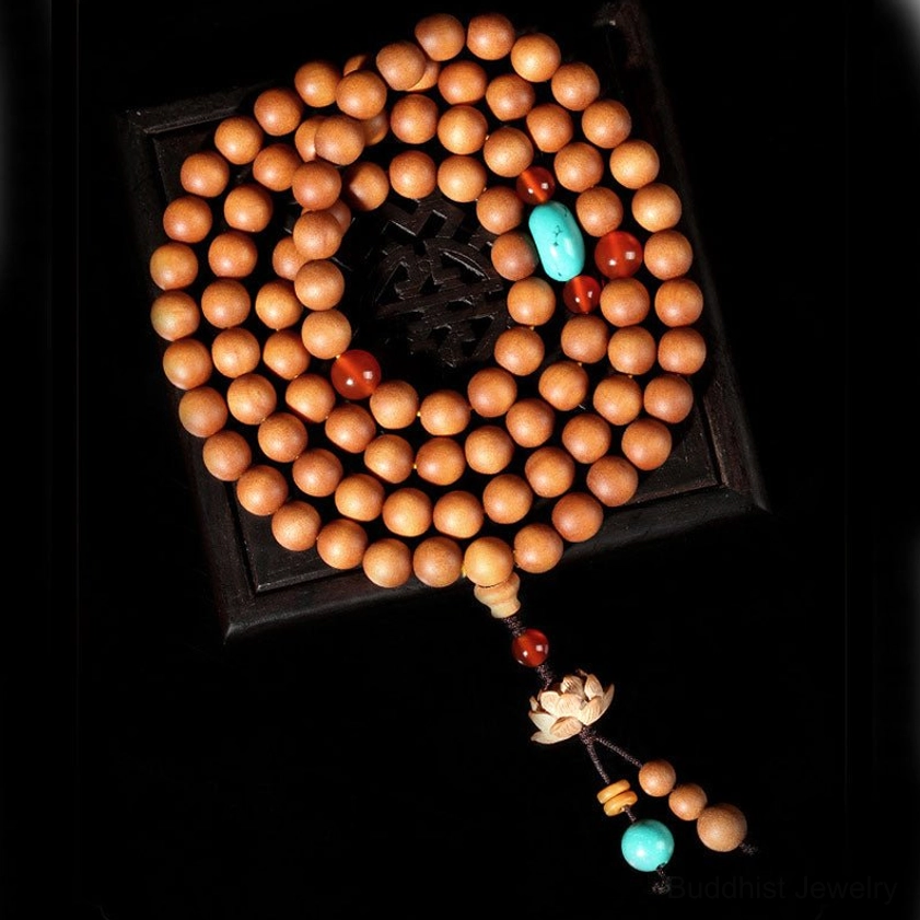 Overhead flat lay of 108 bead Buddhist mala arranged in circle on dark square tray, lotus pendant with turquoise tassel centered