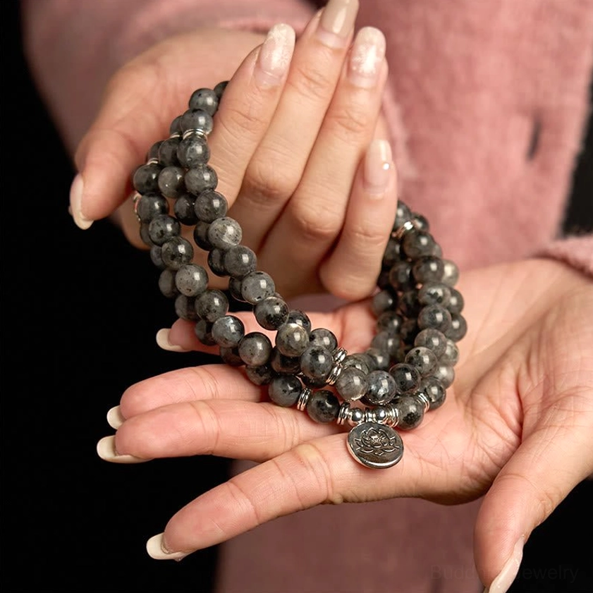 Two hands displaying black glitter stone mala bracelet with lotus charm pendant wearing context