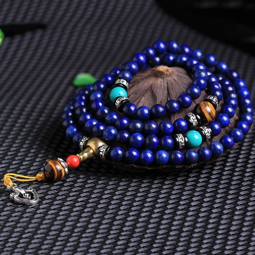 Flat lay photography of lapis lazuli 108 bead mala bracelet with metal clasp pendant and natural stone beads on textured background