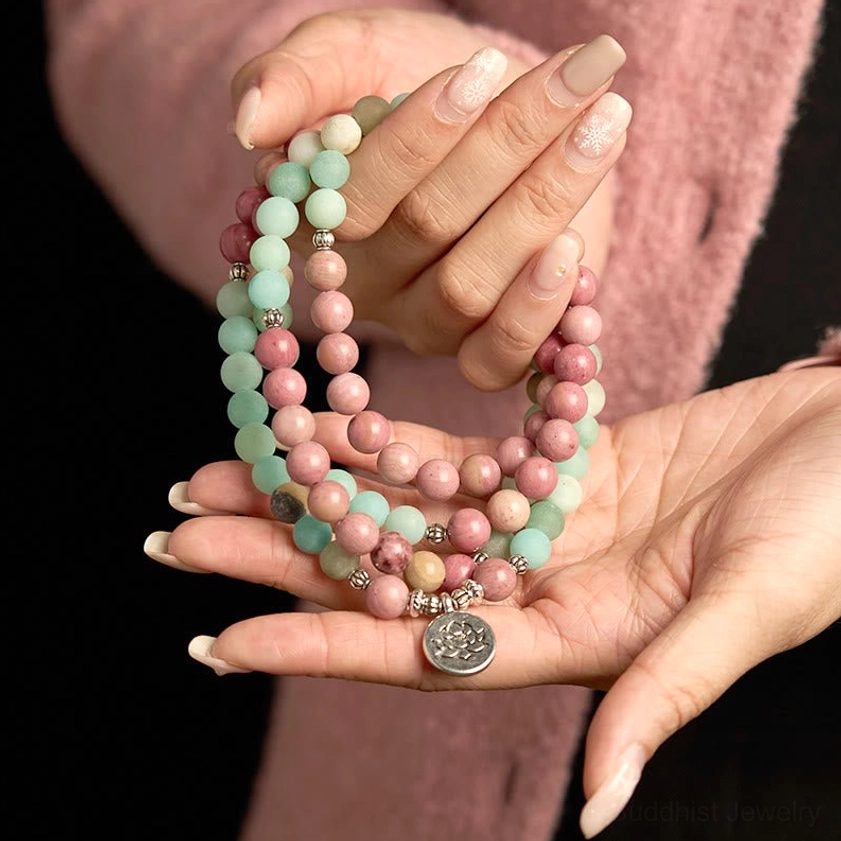 Two hands displaying 108 bead mala bracelet with two-tone stone beads and silver lotus hanging pendant