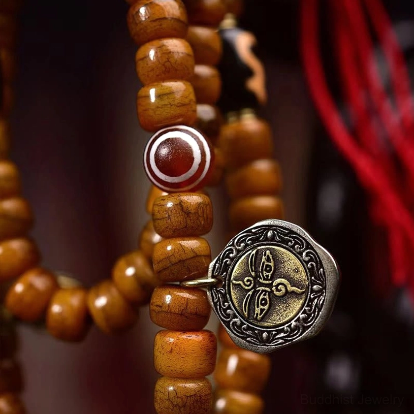 Prayer mala bead strand macro front view featuring brown cylinder bone beads, red agate eye bead, carved metal spiritual pendant, and protective energy details