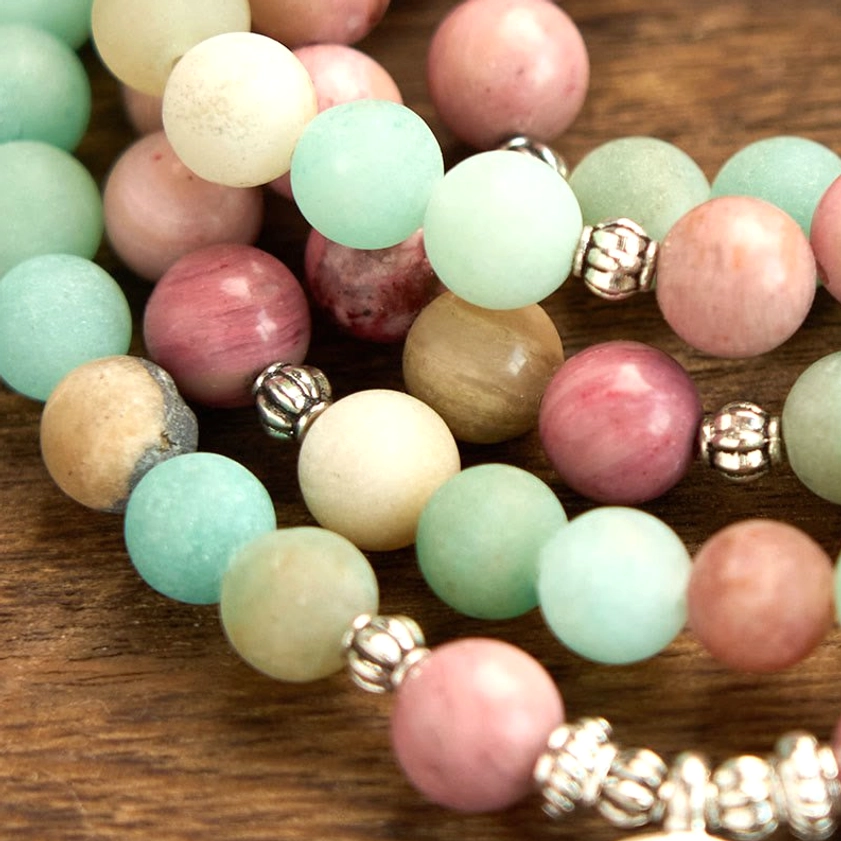 Macro flat lay of 108 mala bead strands showing pink rhodonite, aqua amazonite beads with silver metal accents