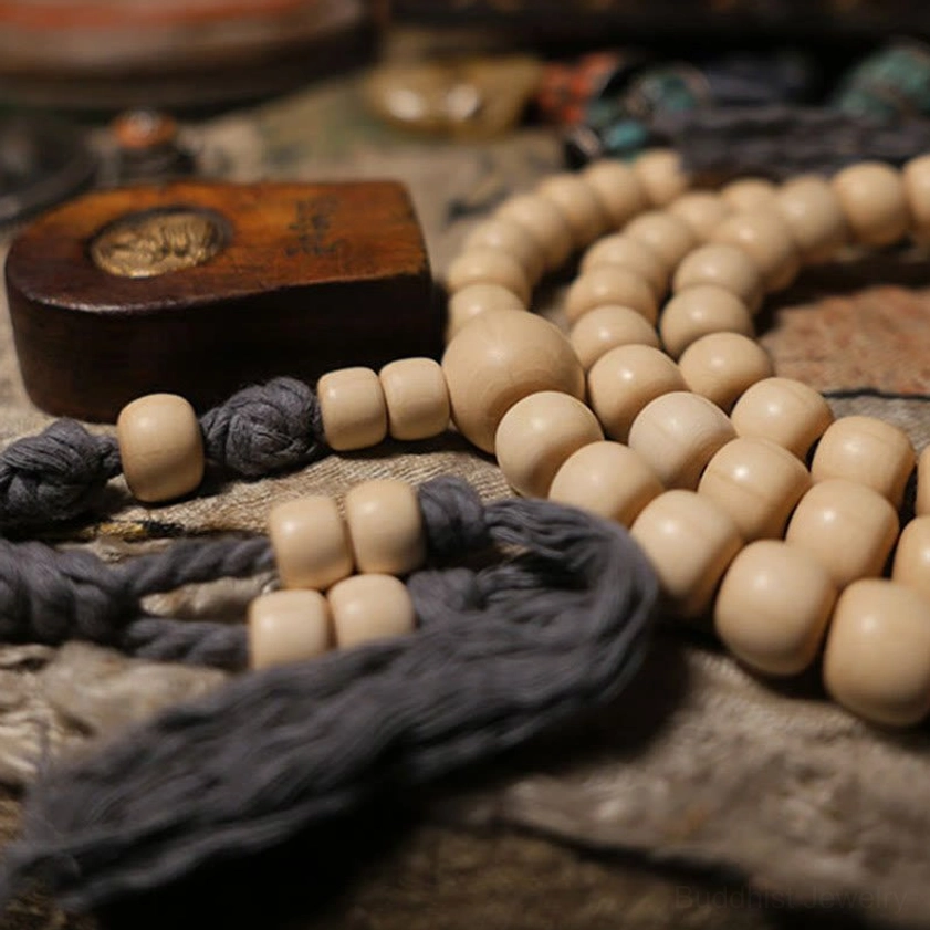 Buddhist prayer mala bracelet with creamy barrel beads displayed next to small Buddha figurine