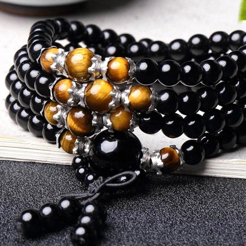 108 bead Buddhist prayer mala flat lay with prominent central black obsidian bead, tiger eye accents and knotted tassel on dark table