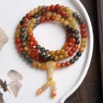 108 bead agate mala bracelet with red agate, yellow agate and black onyx beads displayed on white ceramic plate - top down flat lay view