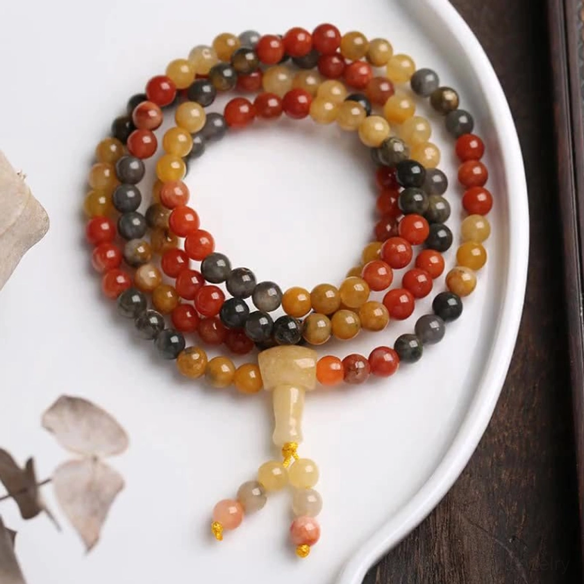 108 bead agate mala bracelet with red agate, yellow agate and black onyx beads displayed on white ceramic plate - top down flat lay view