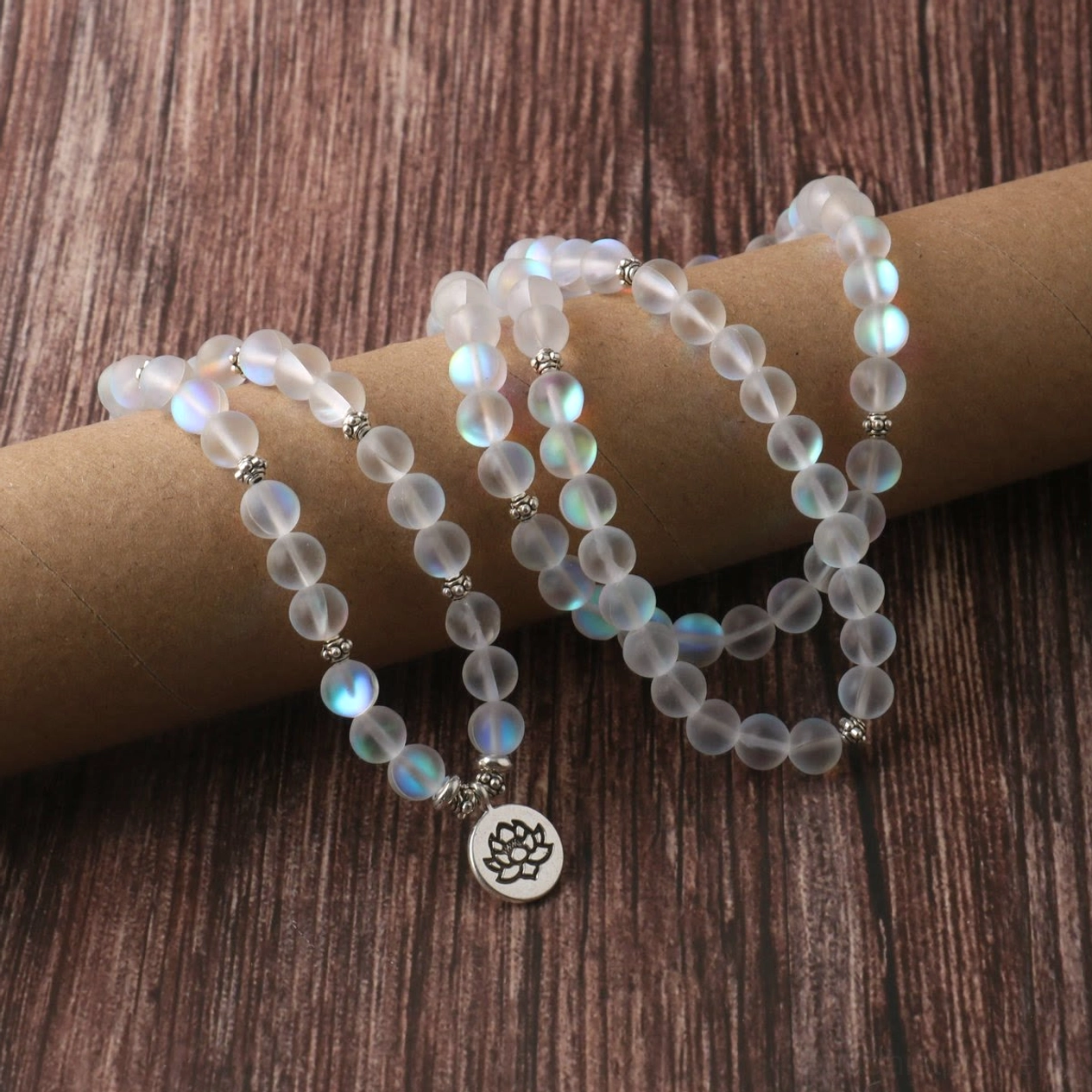 Side angle of 108 mala meditation bracelet showing iridescent frosted beads, loose beaded layout and lotus pendant on dark wooden desktop
