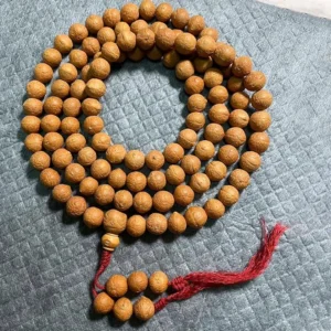 108 Bodhi seed mala beads bracelet with red tassel, overhead view on grey quilted fabric