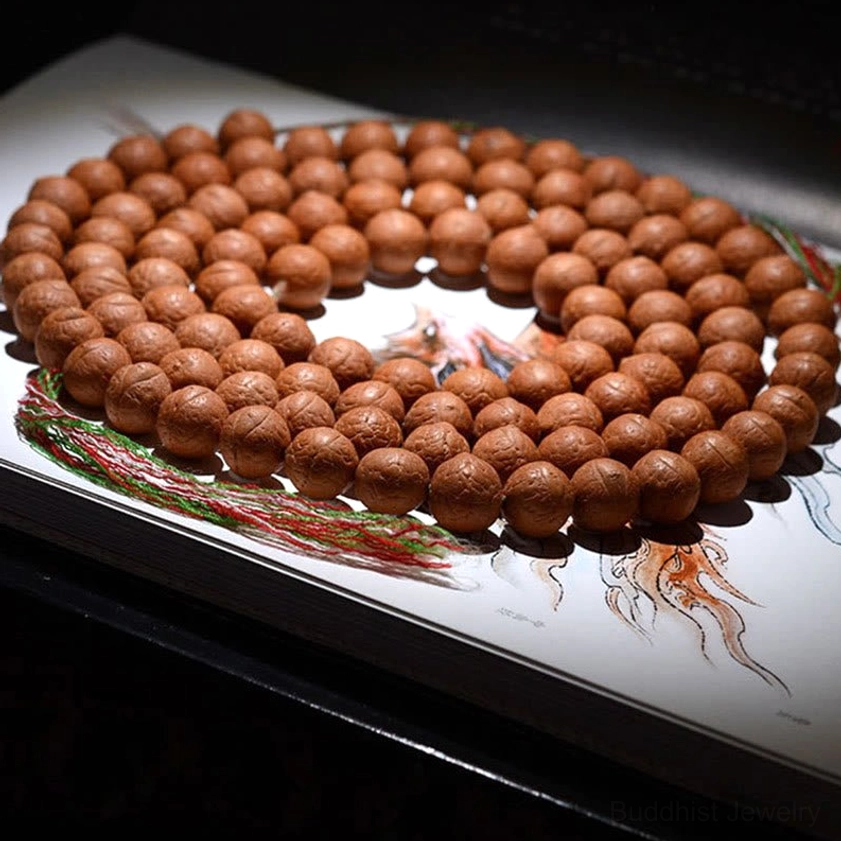 108 Bodhi seed mala beads with red-green tassel on book background, overhead shot