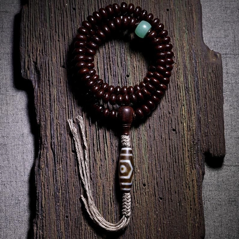108 purple bodhi seed mala with three-eyed dzi bead pendant on wooden background