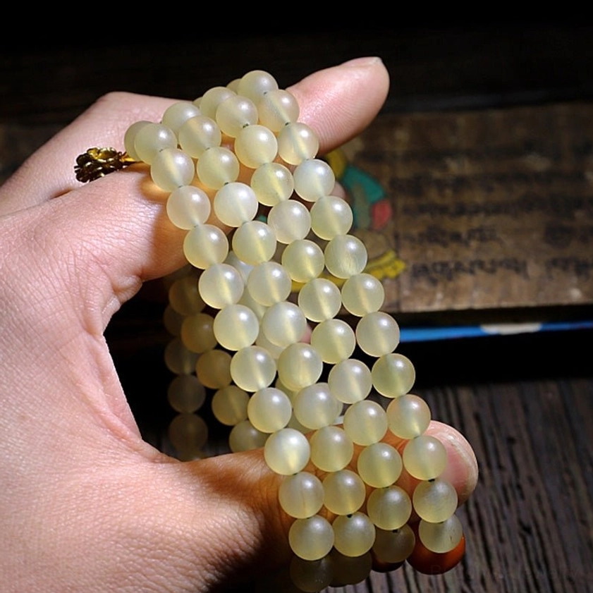 108 mala beads held between fingers showing translucent light yellow sheep horn and carved guru bead detail