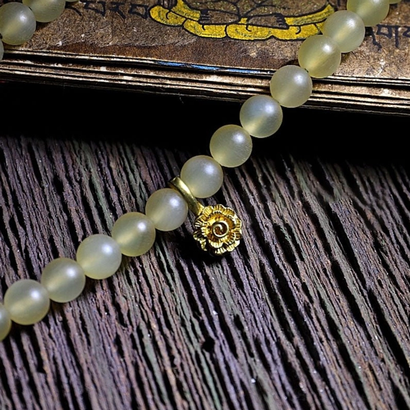 Partial 108 mala prayer beads close-up with round light yellow beads and golden flower charm on Sanskrit wood
