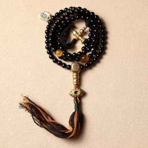 Black onyx 108 mala beads bracelet with tassel pendant and brass guru bead on beige background