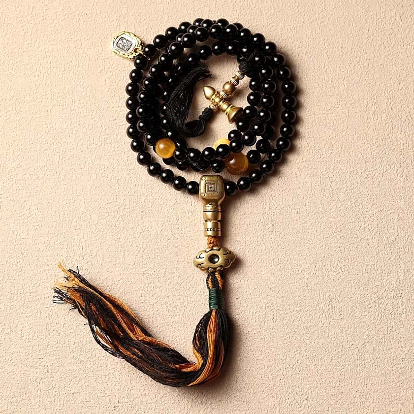 Black onyx 108 mala beads bracelet with tassel pendant and brass guru bead on beige background