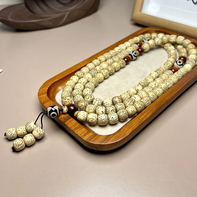 Buddhist prayer mala beads stacked display showing 108 Bodhi seeds with Dzi bead tassel on natural wooden tray
