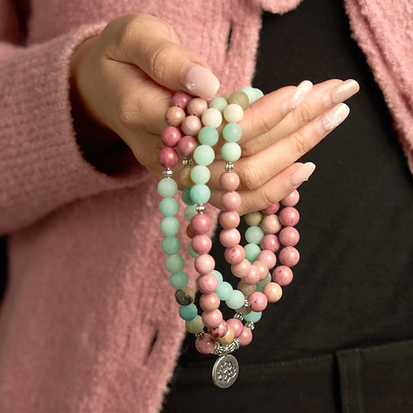 Close-up of 108 mala bead bracelet in palms showing rhodonite pink and amazonite aqua beads with silver lotus charm