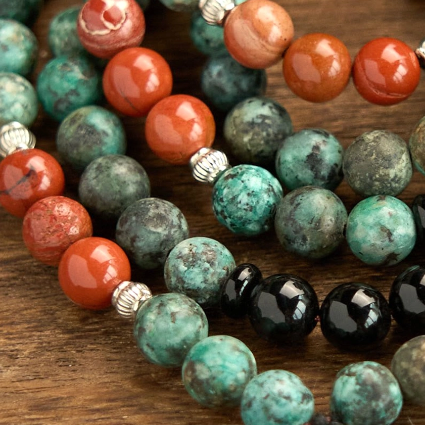 Overhead close-up of 108-bead mala showing natural black onyx, red jasper, and turquoise beads with silver spacer beads and detailed texture