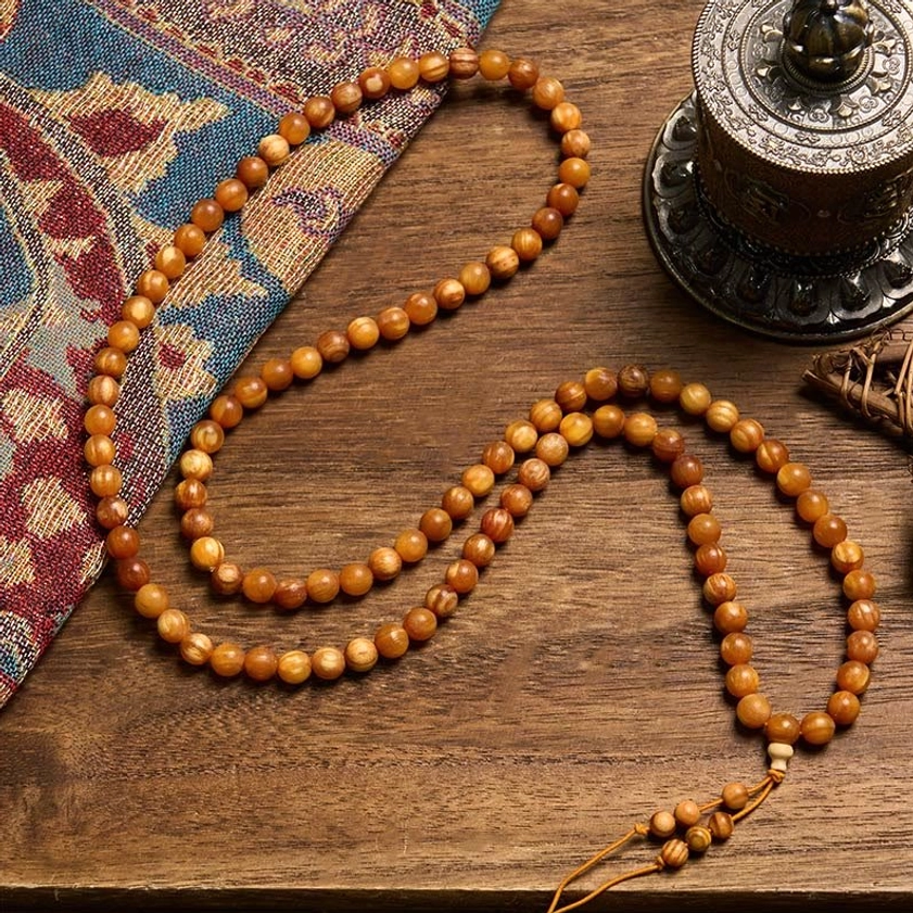 Long strand of natural resin-rich pine wood prayer beads laid flat on patterned cloth and incense setting
