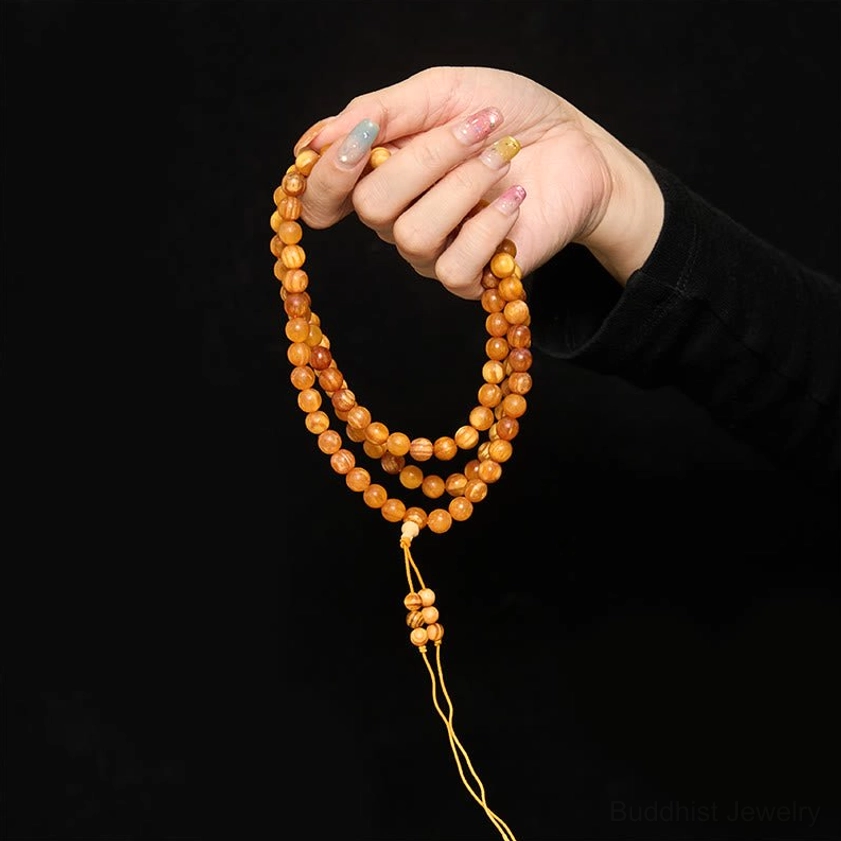 Hand holding single strand of small round resin-rich pine wood mala beads on black background