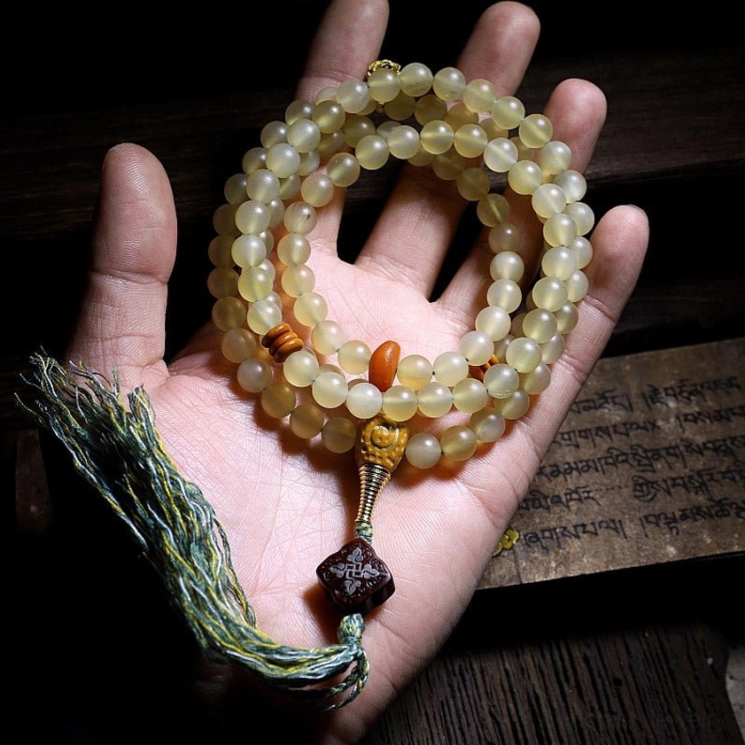 108 prayer mala beads in palm showing light yellow beads with green tassel and dark brown decorative element