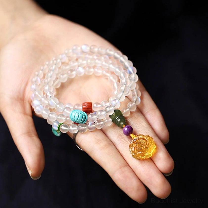 Stacked 108 moonstone mala beads on palm, showing clear translucent beads with carved amber lotus pendant