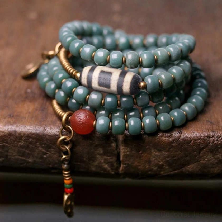 Coiled 108 mala bead set with teal bodhi seeds, protective dzi bead, red agate accent, and brass ornaments close-up