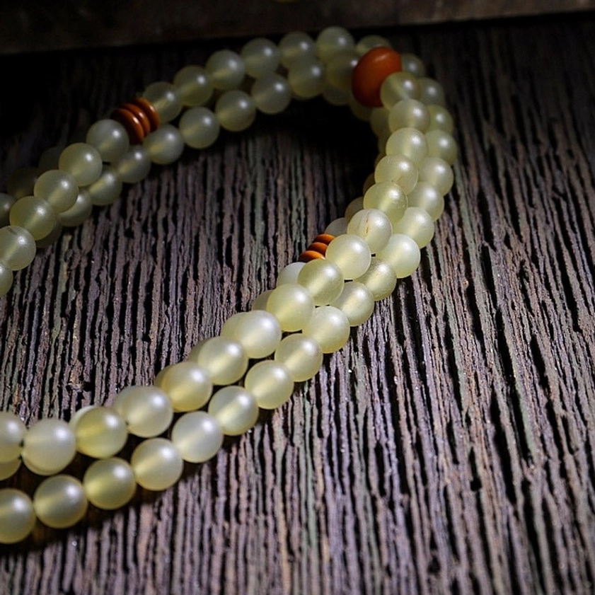 108 mala prayer beads arranged flat on dark wood showing cylindrical light yellow beads and red spacer beads
