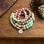 108 bead Buddhist prayer mala bracelet with rhodonite and amazonite stones, silver lotus charm displayed on wooden desk