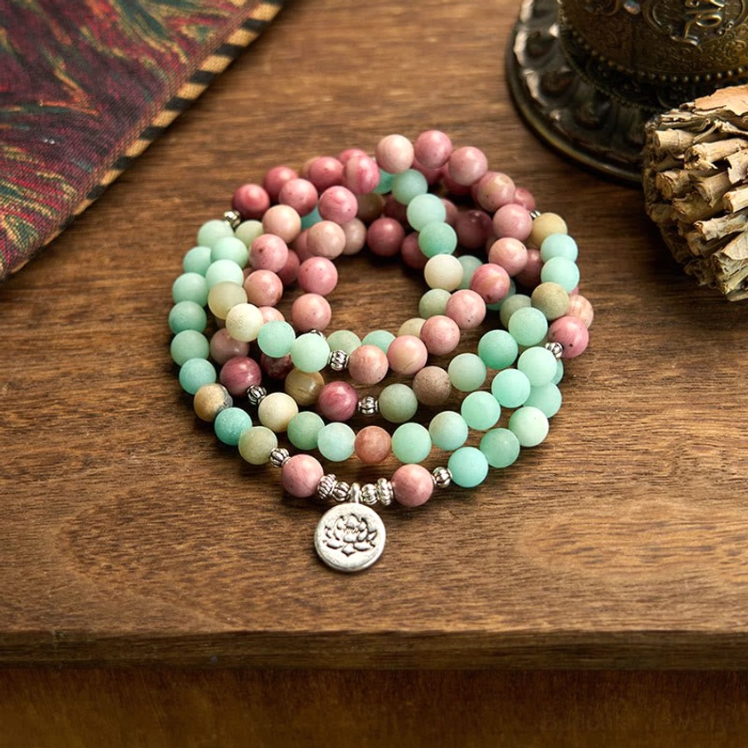 108 bead Buddhist prayer mala bracelet with rhodonite and amazonite stones, silver lotus charm displayed on wooden desk