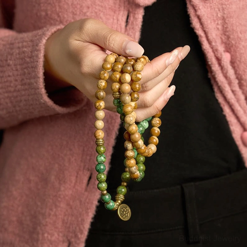 Close-up hand-held view of 108-bead mala bracelet showing natural stone texture with lotus metal pendant
