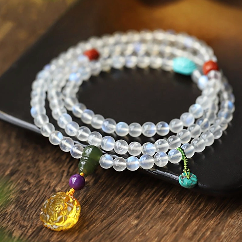 108 moonstone mala bracelet on wooden table with black tray, featuring lotus amber and turquoise pendants