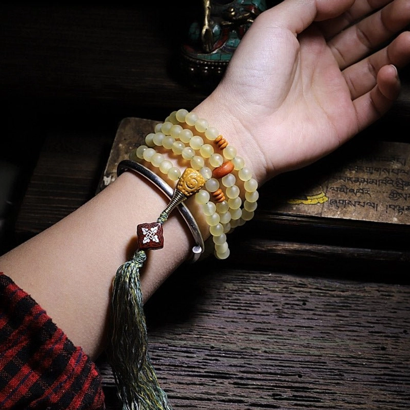 Mala bracelet wrapped on wrist with metal wristband and green tassel showing spiritual jewelry styling