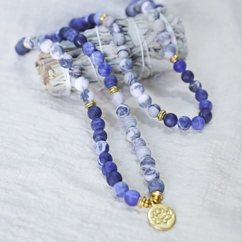 Buddhist mala beads necklace paired with dried sage, spiritual wellness arrangement, blue and white stone beads with gold lotus charm