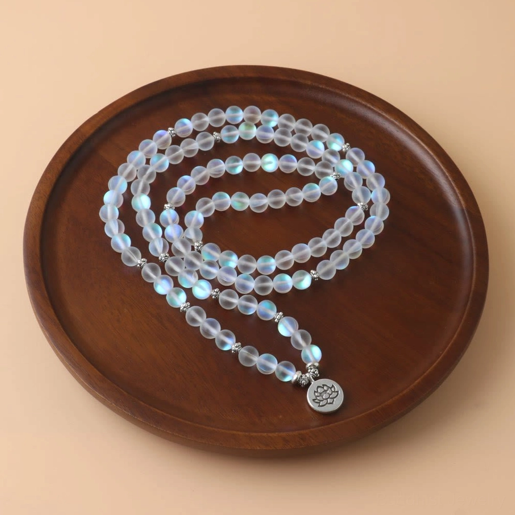 Top-down view of 108 mala meditation bracelet featuring iridescent frosted beads, silver lotus pendant charm on light wooden round tray
