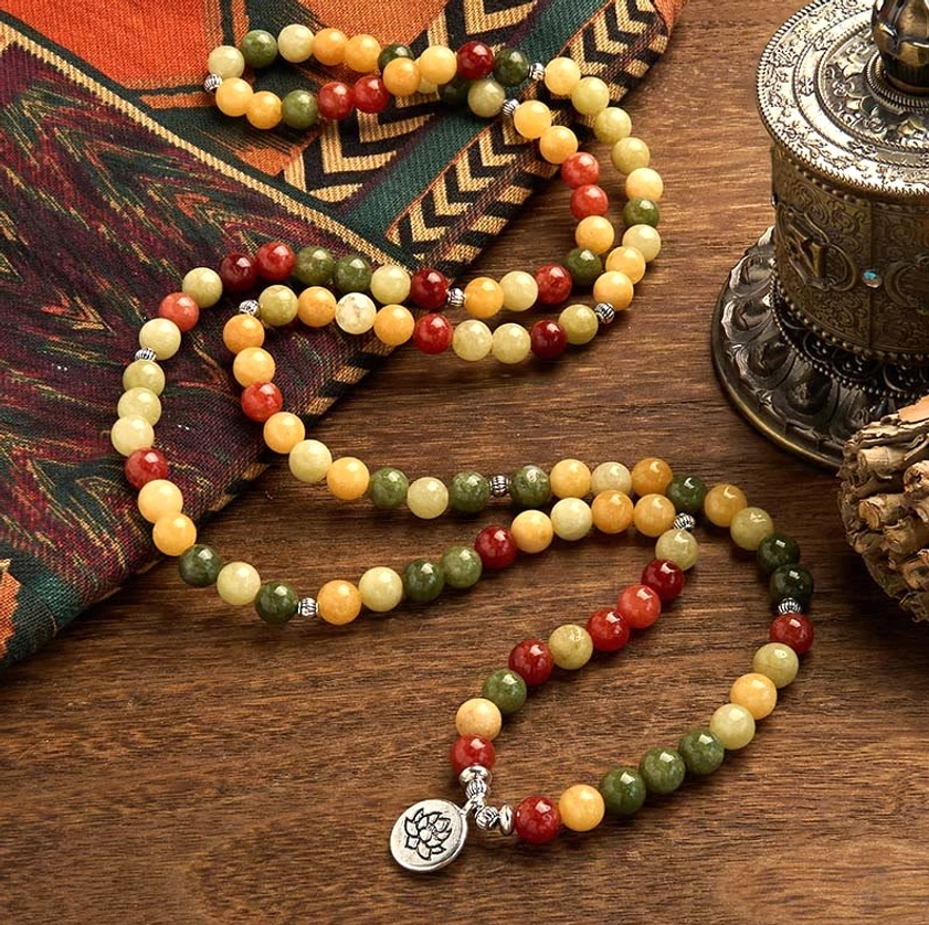 Handmade 108 prayer bead mala bracelet featuring mixed natural colored gemstone beads and silver lotus metal pendant on ethnic fabric