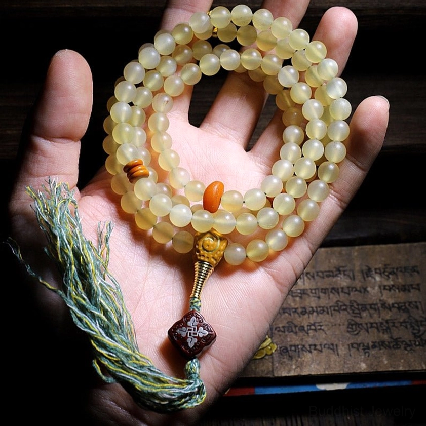 108 mala beads held in palm showing light yellow sheep horn beads with green tassel and red decorative bead