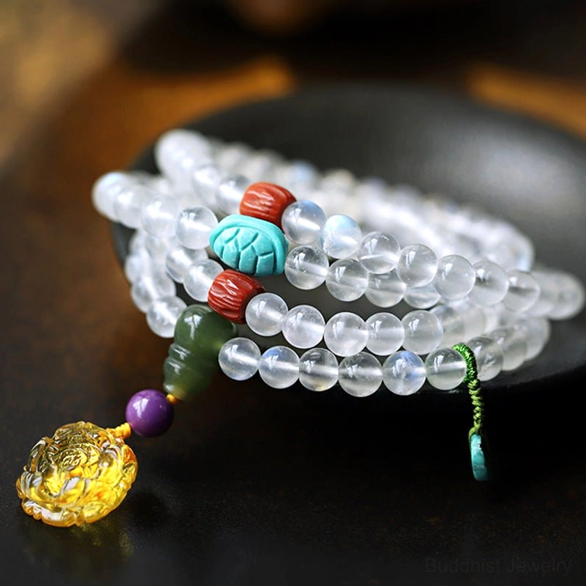 Buddhist 108 mala prayer beads stacked on black ceramic plate, showing turquoise and gemstone accents with lotus pendant