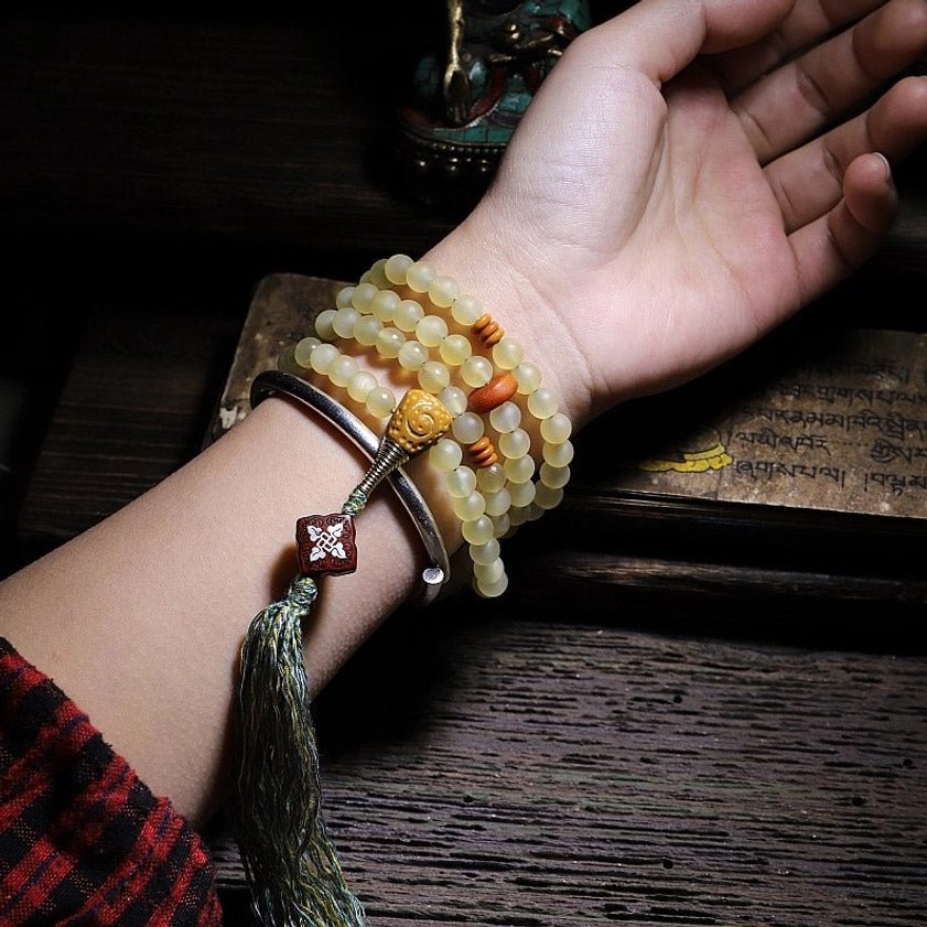 Buddhist mala bracelet on wrist with metal band and dark grey tassel for meditation practice