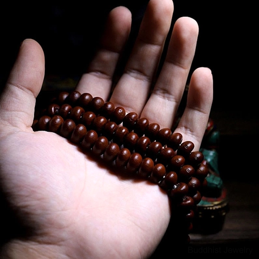 Full 108-bead mala strand in palm showing purple bodhi seeds and Buddhist ornaments