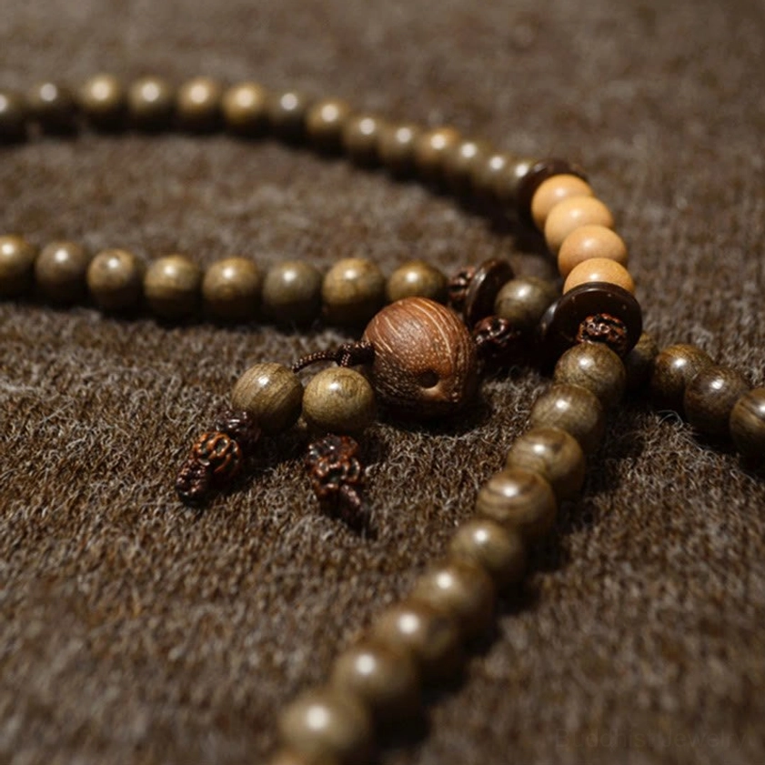 Long sandalwood Buddhist prayer beads with dark olive and light brown wood beads, central tassel pendant, overhead view on textured background