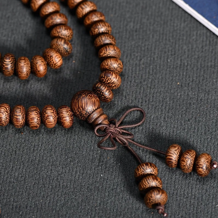 Side close-up of natural wood bead mala strand with fine grain texture and multi-piece tassel