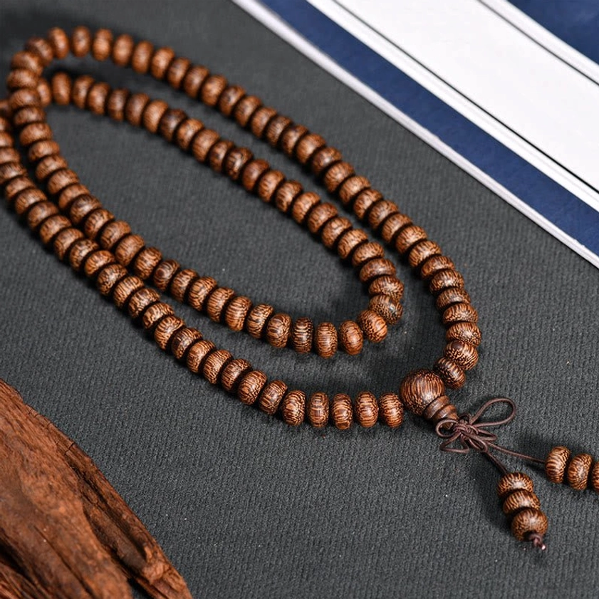 Long wooden prayer bead mala necklace loosely laid with decorative knot and tassel, flat lay view
