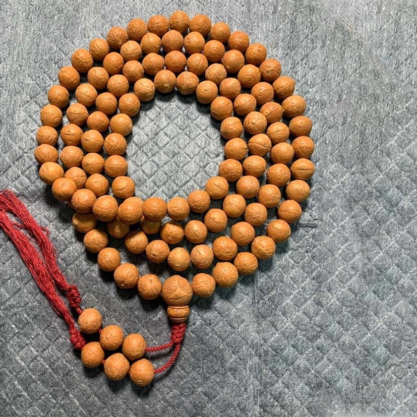 12mm Bodhi seed mala bracelet with red fabric tassel and wooden guru bead, grey fabric backdrop