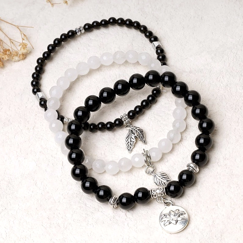 3-piece beaded healing bracelet set with black and white stone beads and silver charm pendants on decorative botanical background