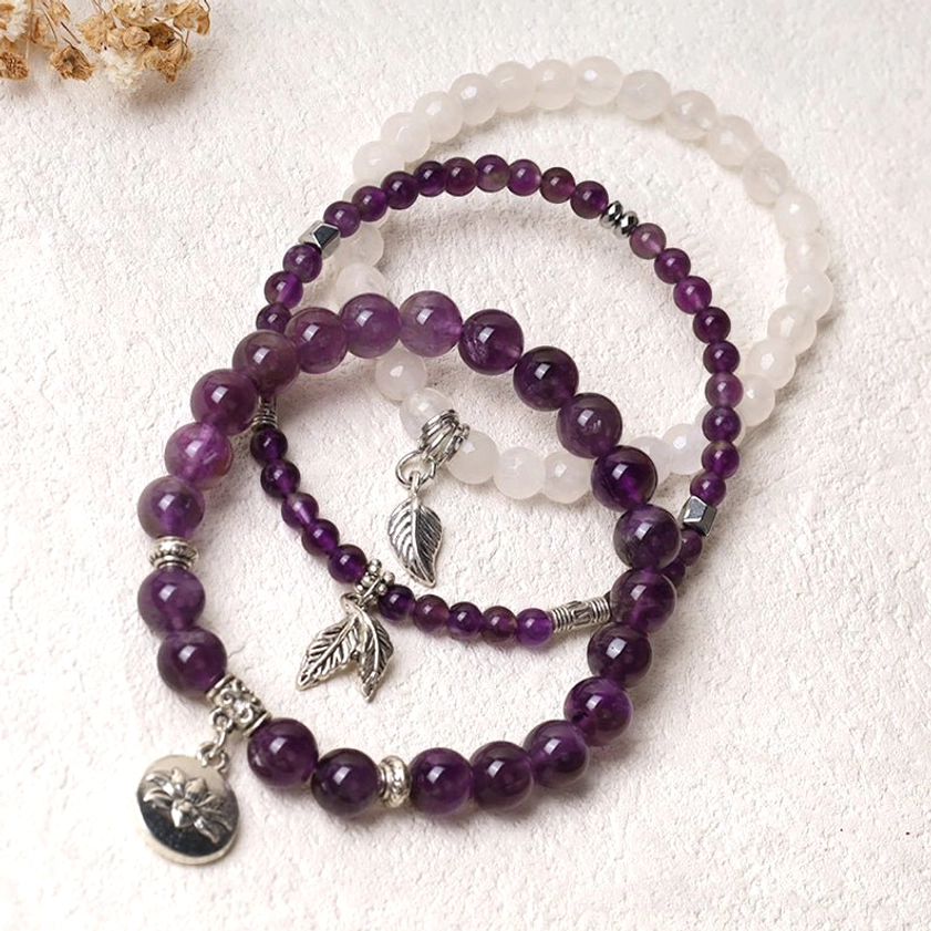 3-piece natural gemstone healing bracelet collection with dark purple amethyst, white quartz and silver pendants on botanical background