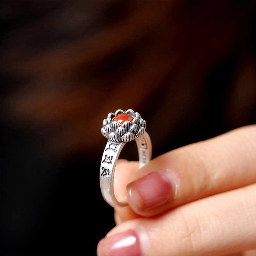 Sterling silver lotus red agate ring handheld close-up with sutra engraving and pink manicure background