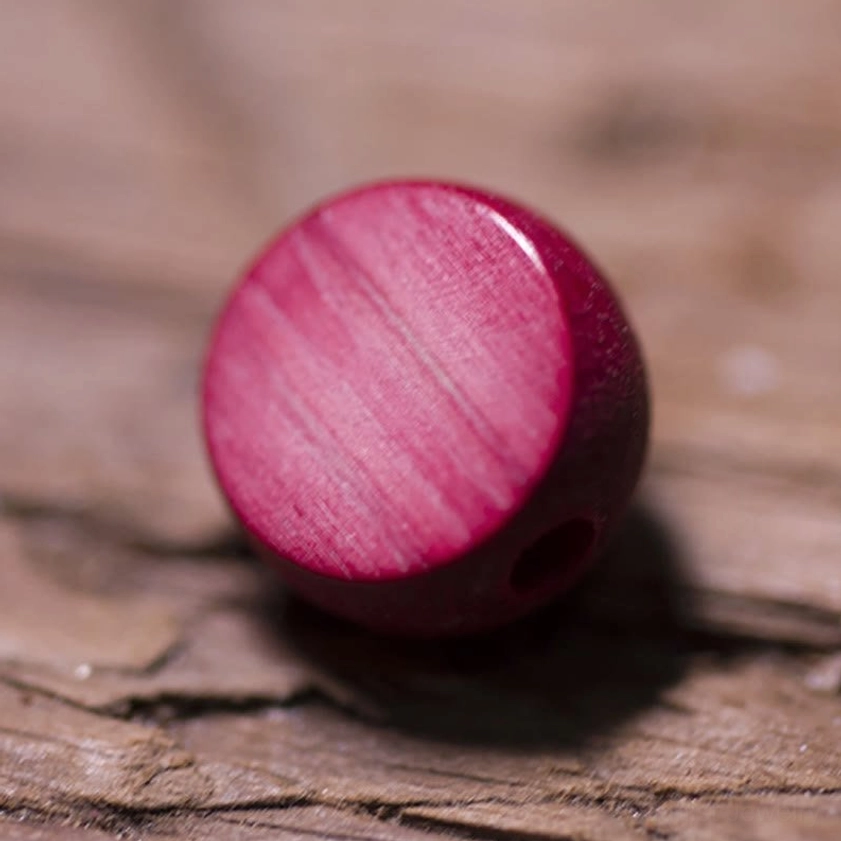 Single Abelia Biflora guru bead showing deep red stain and visible natural wood grain texture with drilled hole